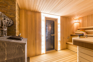 Traditional wooden sauna with benches. Heating element. A glass door illuminated around the perimeter.