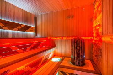 Traditional wooden Finnish sauna with red lighting. The heating element of the original shape.