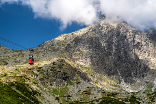Tatranska Lomnica, Slovakia – June 21, 2025: Red cable car ascending to Lomnicky stit peak in High Tatras mountains with dramatic rocky slopes and cloudy summit.