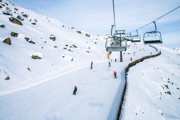 A winter ski resort in the mountains with people skiing down snowy slopes and a modern ski lift. The concept is active winter recreation, outdoor sports, and mountain travel.