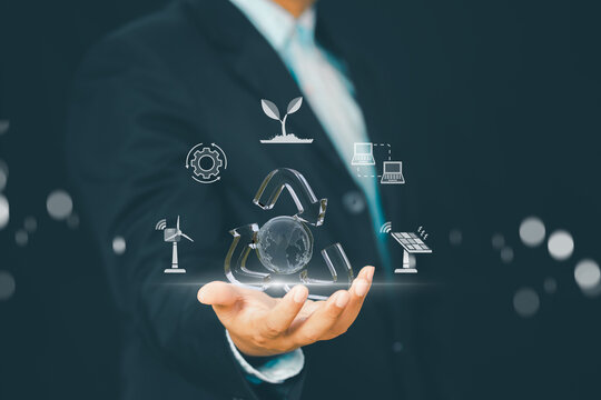 Sustainable business concept with businessman holding holographic recycling globe and renewable energy icons, symbolizing green technology, clean energy solutions, and eco-friendly corporate strategy.