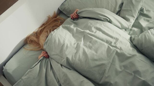 Tired woman struggling to fall asleep in bed and covers herself with blanket