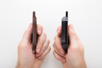 Man hands holding new and old rusty brake pads on light gray table background. Showing thick and...