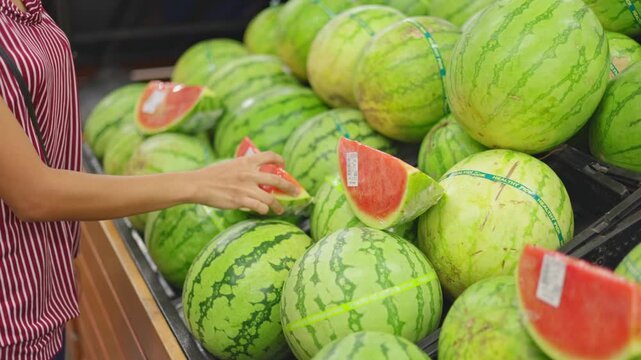 Shopper inspects ripe watermelon grocery store shelf, shopper taps melon for quality display with fresh produce, vibrant fruit selection scene, quality check prep, ideal fresh market haul content.