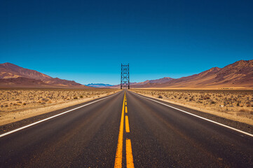 Endless desert highway leading to a distant tower under a clear blue sky