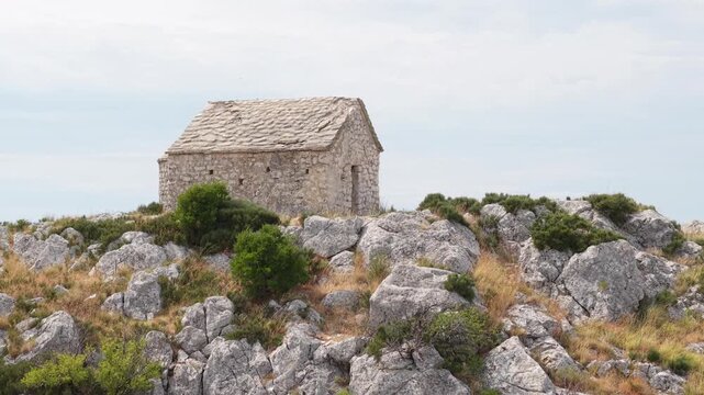 Ancient stone chapel on a coastal mountain ridge with panoramic sea view of the Dalmatian coast.