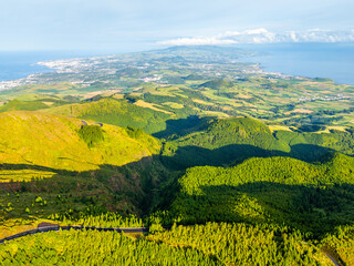 Fototapeta premium Green Hills, Pasturelands and Forest on Sunny Morning. Atlantic Ocean. Azores, Sao Miguel Island, Portugal. Aerial View