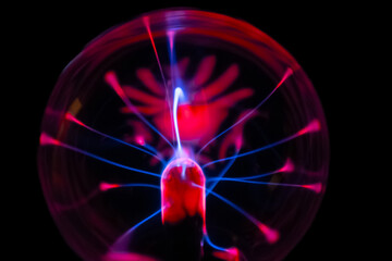 A vivid plasma ball glows in the dark, with electric pink and blue arcs radiating from its center,...