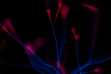 Vivid electric blue and red arcs leap from the core of a plasma lamp, creating a dazzling display of energy against a pitch-black background.