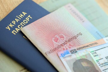 German Permanent resident card and document specimen lies with Ukrainian passport on wooden table