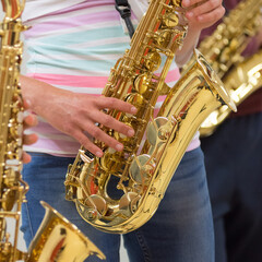 Human hand holding playing a saxophone close up with another saxophone in the background during musiclessons