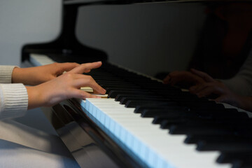 Human hands playing the keys notes and chords on a classic black piano during a pianolesson