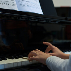 Human hands playing the keys notes and chords on a classic black piano during a pianolesson