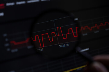 Magnifying glass observing dynamic red line graph on dark digital screen, reflecting market data, financial volatility, stock analysis, and economic trends