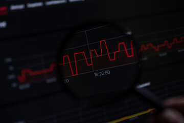 Magnifying glass analyzing a volatile red line graph on screen, signifying critical data...