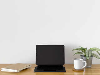 Black laptop sits on a wooden desk with a white mug and a potted plant