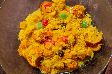 Steamed couscous with dried hands, nuts, and turmeric in a transparent bowl. Horizontal photo.