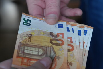 Close-up of a Financial Transaction: One Person Handing Over Multiple €50 Euro Banknotes to Another, Symbolizing Payment and Exchange