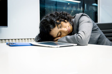 Exhausted young businesswoman with curly hair working hard overtime, sleeping in office desk. Tired...