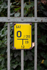 Yellow gas sign on metal fence surrounded by green foliage in an urban setting