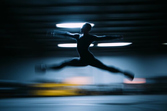 Ballet dancer mid leap in industrial warehouse with dramatic lighting and motion blur