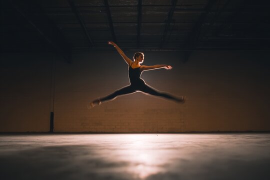 Ballet dancer mid leap in industrial warehouse with dramatic lighting and motion blur
