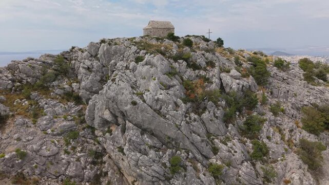 Ancient stone chapel on a coastal mountain ridge with panoramic sea view of the Dalmatian coast.