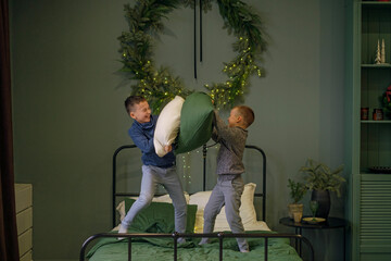 The boys are having fun in their parents' bedroom, playing on the bed, fighting with pillows. The room is decorated with wreaths and garlands for Christmas and New Year
