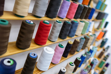 Spools of thread of various colors neatly arranged on wooden shelves, creating a visually appealing display for sewing and tailoring projects or facilities.