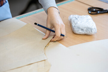 A fashion designer, cutter, or dressmaker working with paper sewing patterns on a large table. A concept of the creative process and handmade clothing design.