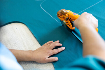 A cutter or pattern cutter uses an electric rotary cutter to cut through a stack of fabric in a garment factory. A concept of the textile industry and mass production.