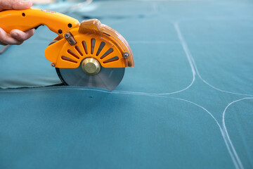 A cutter or pattern cutter uses an electric rotary cutter to cut through a stack of fabric in a...