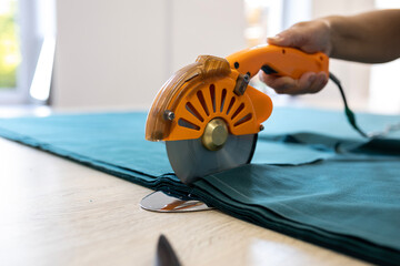A cutter or pattern cutter uses an electric rotary cutter to cut through a stack of fabric in a garment factory. A concept of the textile industry and mass production.