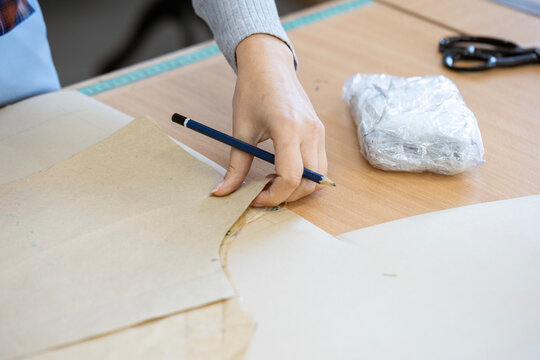 A fashion designer, cutter, or dressmaker working with paper sewing patterns on a large table. A concept of the creative process and handmade clothing design.