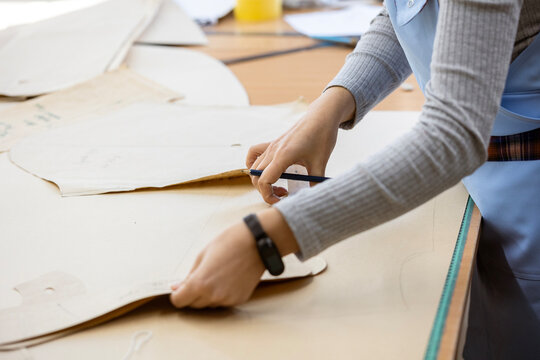 A fashion designer, cutter, or dressmaker working with paper sewing patterns on a large table. A concept of the creative process and handmade clothing design. - Powered by Adobe