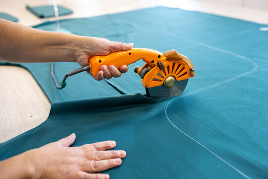 A cutter or pattern cutter uses an electric rotary cutter to cut through a stack of fabric in a garment factory. A concept of the textile industry and mass production.