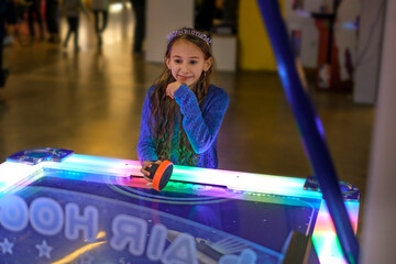 A cute laughing girl plays table air hockey at the entertainment fair center on her birthday