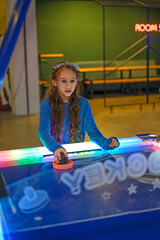 Focused on the game and competition, a girl plays table air hockey in an amusement park