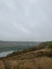 Misty autumn morning with fog over a calm pond surrounded by colorful trees on gentle hills. Peaceful natural landscape in soft light.