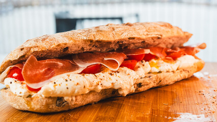 A beautiful closed ciabatta sandwich filled with creamy burrata, delicate prosciutto, and fresh cherry tomatoes. Ready to eat and bursting with Italian flavors in every bite.