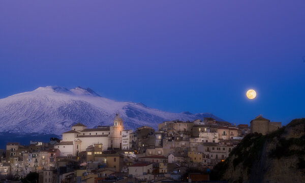 A small town Centuripe with a church and a vulcano Etna in the background. The moon is shining brightly in the sky
