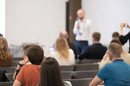 Audience listens to speaker presenting at conference. Blurred stage, attentive attendees, devices in use, learning professional event - Powered by Adobe