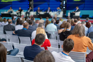 Crowd attends panel discussion at large conference with experts on stage delivering insights, audience seated in rows listening attentively to industry leaders
