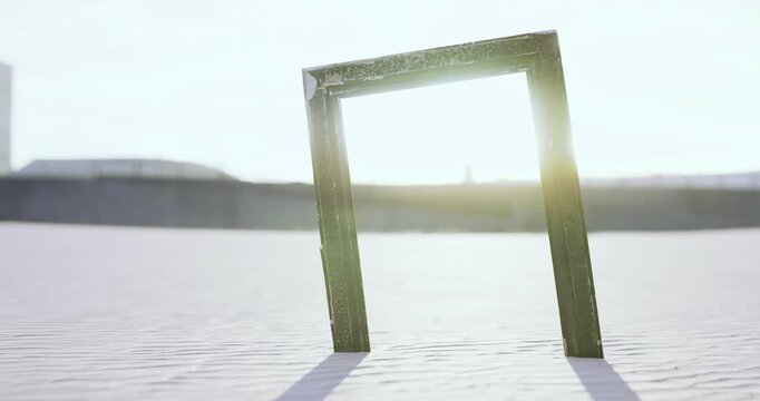 A wooden frame stands alone on a sunlit beach, casting long shadows on the smooth sand. The sun sets in the background, creating a dreamy atmosphere of solitude and reflection.
