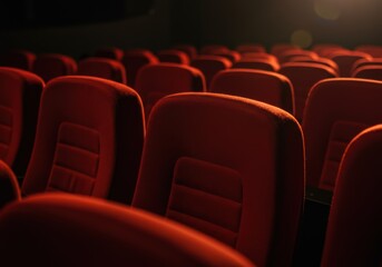 Obraz premium Rows of red theater seats illuminated by soft lighting in a darkened auditorium.