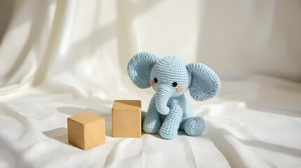 Charming blue handcrafted knitted elephant toy placed alongside wooden blocks on a sunny white fabric, evoking a sense of warmth and creativity.