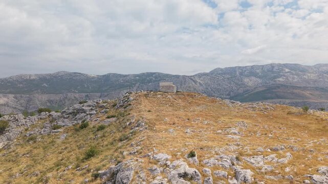 Ancient stone chapel on a coastal mountain ridge with panoramic sea view of the Dalmatian coast.