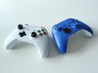 Two modern game controllers, white and blue, rest on a clean, pale surface. Ideal stock imagery for gaming, accessories, and entertainment topics emphasizing collaboration, play, and digital fun.