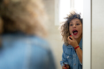 Woman applying red lipstick in bathroom mirror reflecting