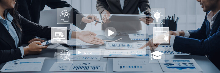 A business team collaborates in a modern office environment, discussing important analytics data with charts while technology icons provide a visual overlay. Trope